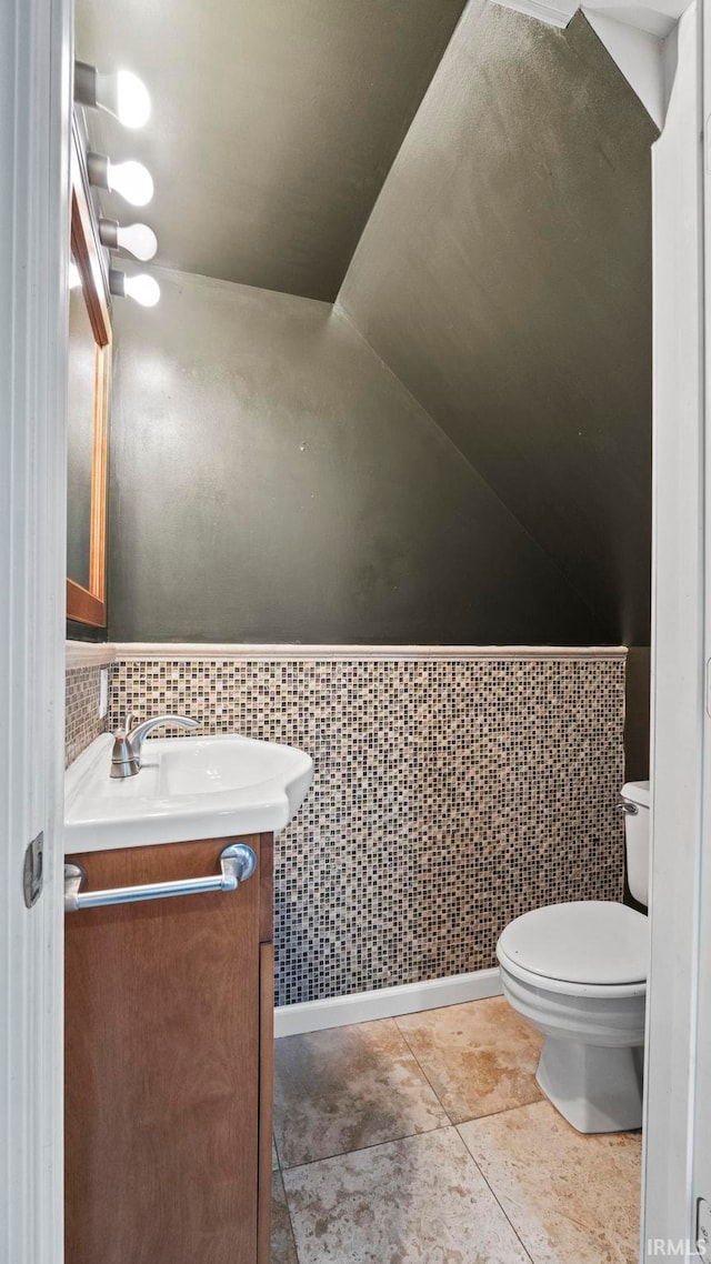 half bathroom featuring toilet, tile patterned flooring, lofted ceiling, and vanity