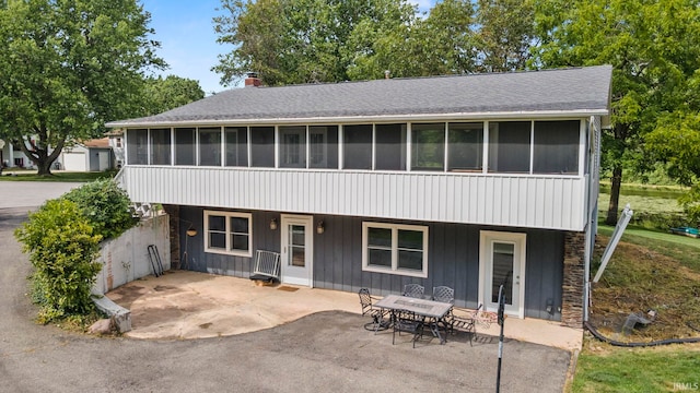 view of front of home with a sunroom, a shingled roof, a chimney, and a patio