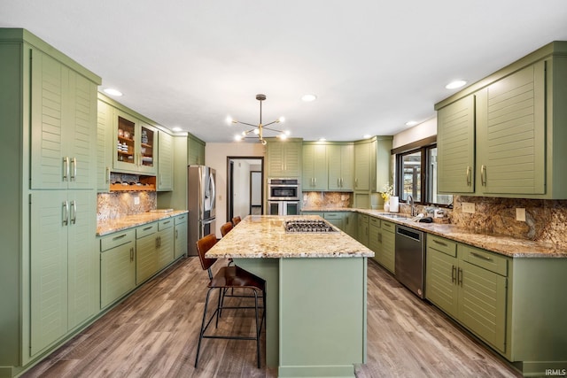 kitchen featuring wood finished floors, a kitchen island, appliances with stainless steel finishes, a kitchen bar, and green cabinetry