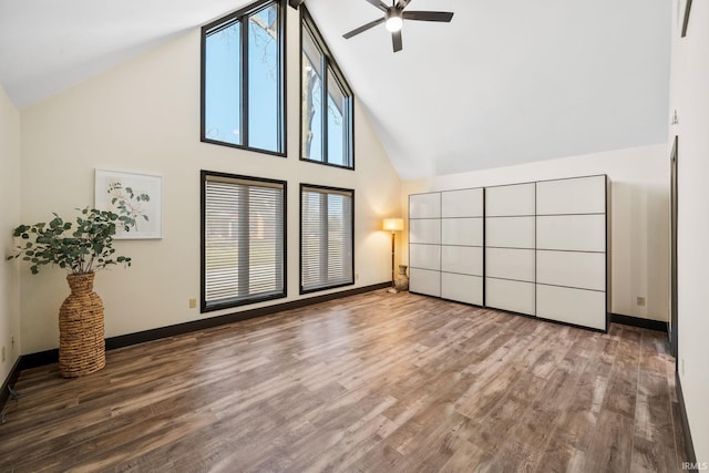 interior space with baseboards, high vaulted ceiling, and wood finished floors