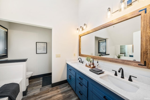 bathroom featuring double vanity, a sink, toilet, and wood finished floors