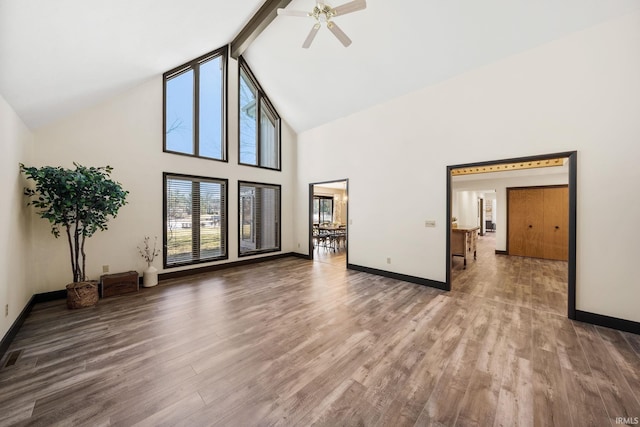 unfurnished living room featuring high vaulted ceiling, beamed ceiling, wood finished floors, and baseboards