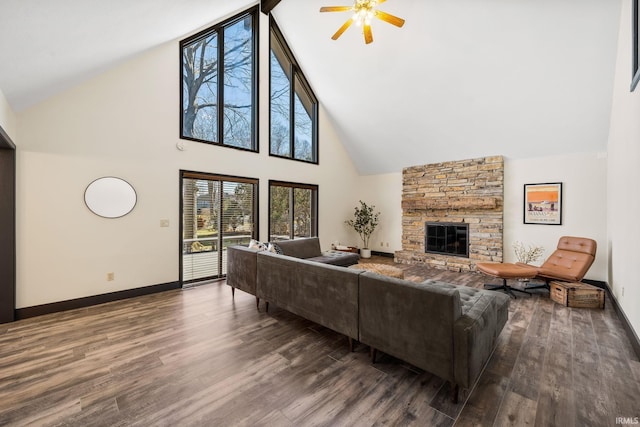 living area featuring ceiling fan, a stone fireplace, baseboards, and wood finished floors