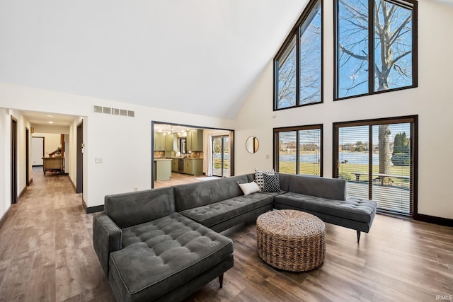 living room with high vaulted ceiling, wood finished floors, visible vents, and baseboards