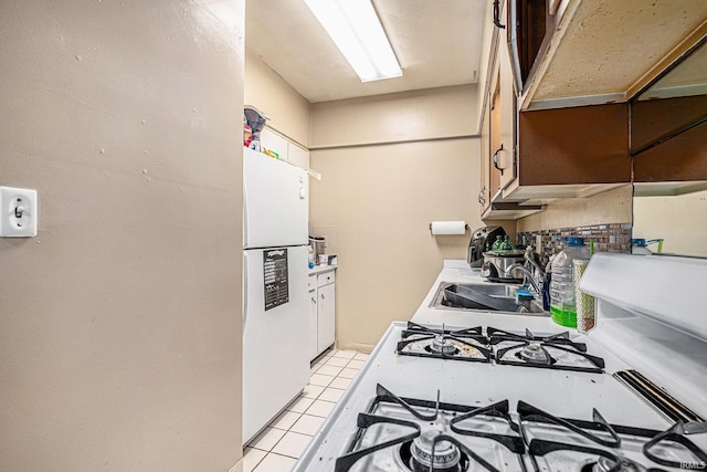 kitchen with gas range, freestanding refrigerator, light countertops, a sink, and light tile patterned flooring