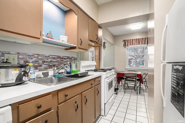 kitchen with light countertops, backsplash, light tile patterned flooring, a sink, and white appliances