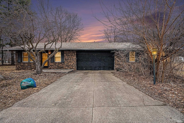 ranch-style home with a garage, concrete driveway, roof with shingles, and brick siding