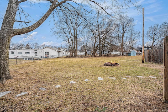 view of yard with a fire pit, a shed, an outbuilding, and fence