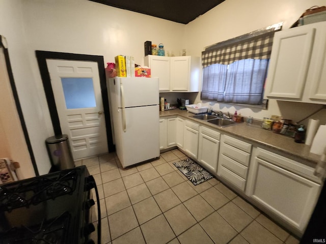 kitchen with light tile patterned floors, freestanding refrigerator, white cabinets, black range with gas cooktop, and a sink