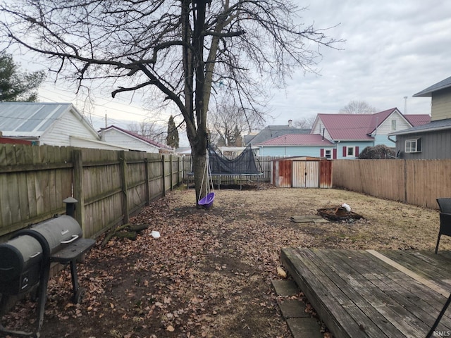 view of yard with a trampoline, an outbuilding, a fenced backyard, and a storage unit