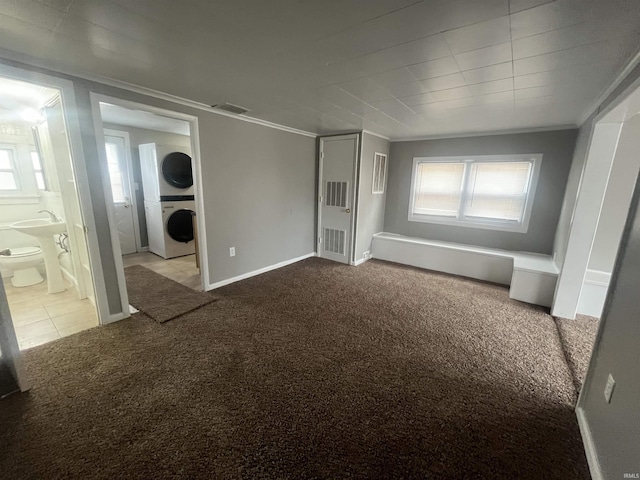 unfurnished bedroom featuring stacked washer and dryer, carpet flooring, visible vents, baseboards, and ornamental molding