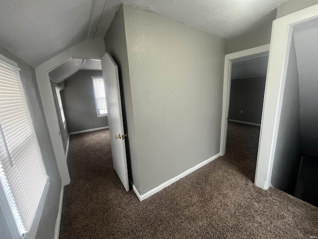 hallway featuring lofted ceiling, carpet floors, a textured ceiling, and baseboards