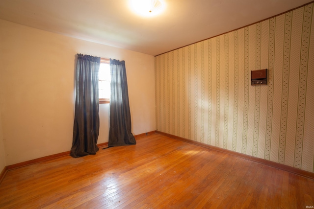 empty room with wallpapered walls, light wood-style flooring, and baseboards