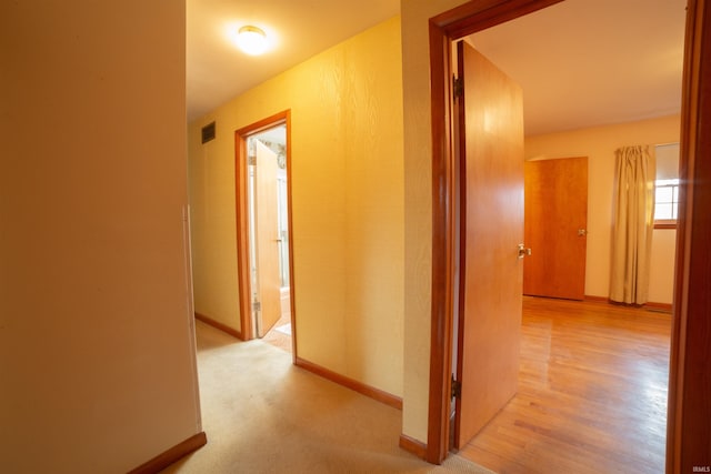 hallway featuring light wood-style floors, visible vents, and baseboards