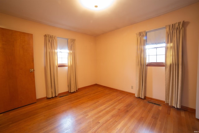 unfurnished room with a wealth of natural light, light wood-type flooring, visible vents, and baseboards