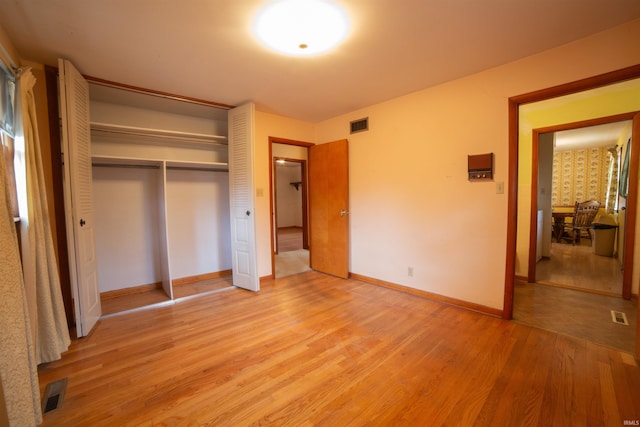 unfurnished bedroom featuring light wood-type flooring, a closet, visible vents, and baseboards