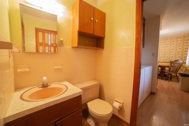 half bathroom with a wainscoted wall, toilet, vanity, wood finished floors, and washer and dryer