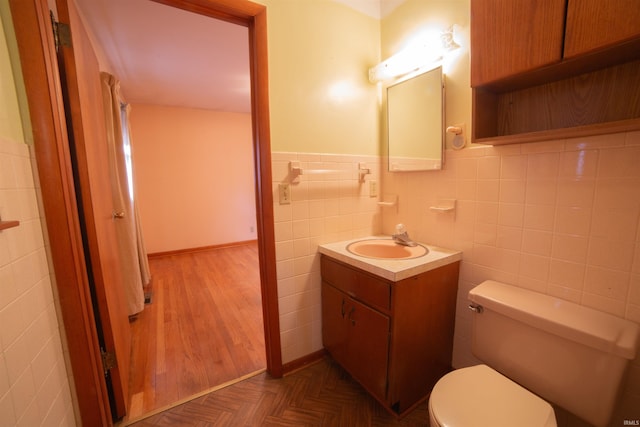 bathroom featuring toilet, a wainscoted wall, tile walls, and vanity