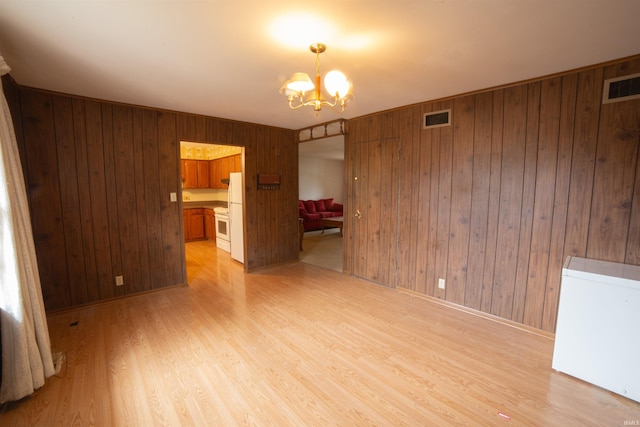 spare room featuring wood walls, light wood-style flooring, visible vents, and a notable chandelier