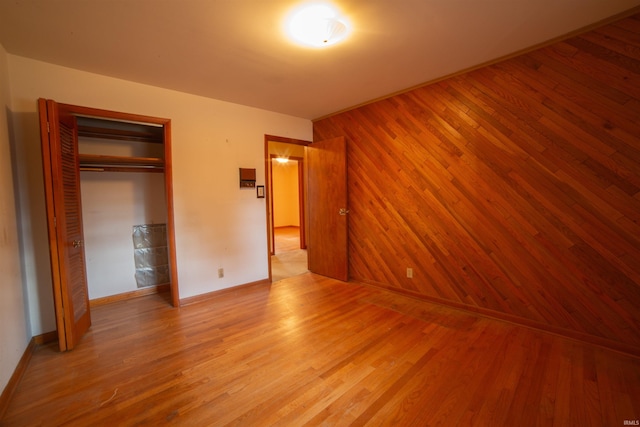 unfurnished bedroom featuring a closet, wooden walls, baseboards, and wood finished floors