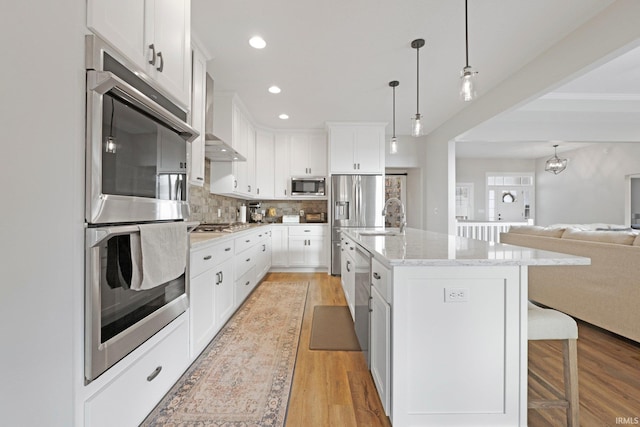 kitchen with tasteful backsplash, light wood-style flooring, appliances with stainless steel finishes, open floor plan, and a kitchen breakfast bar