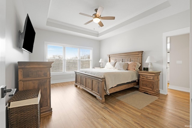 bedroom featuring a tray ceiling, baseboards, ceiling fan, and light wood finished floors