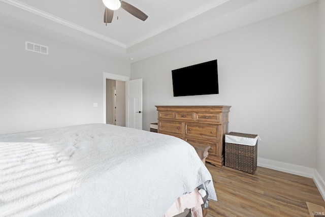 bedroom with crown molding, a raised ceiling, visible vents, wood finished floors, and baseboards