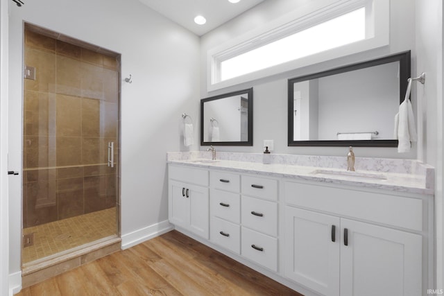 full bath with double vanity, a shower stall, a sink, and wood finished floors