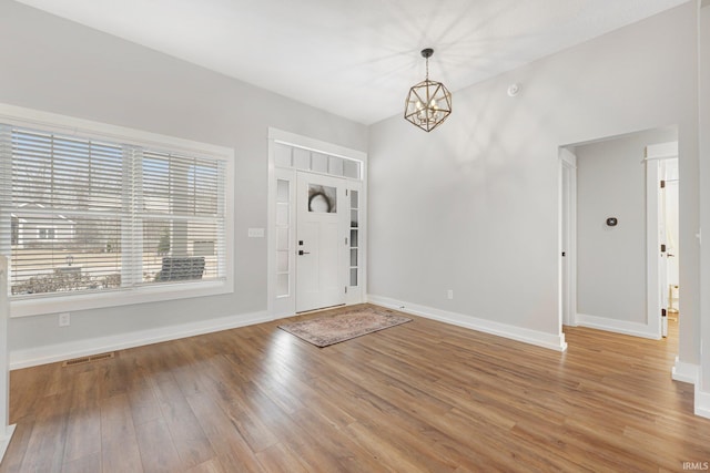 foyer featuring baseboards, wood finished floors, visible vents, and a notable chandelier