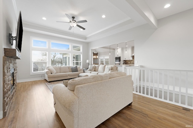 living room featuring recessed lighting, a raised ceiling, a ceiling fan, a stone fireplace, and hardwood / wood-style floors