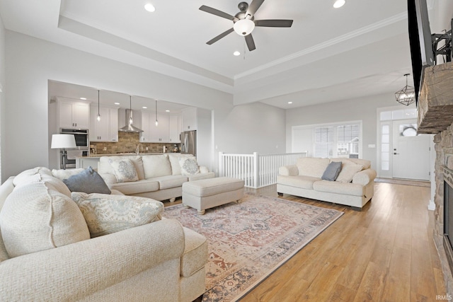 living area with recessed lighting, a fireplace, a ceiling fan, light wood-type flooring, and a raised ceiling