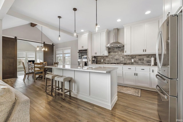 kitchen featuring backsplash, vaulted ceiling with beams, stainless steel appliances, wall chimney range hood, and a sink