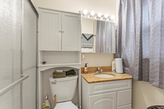 bathroom featuring toilet, a shower with shower door, and vanity