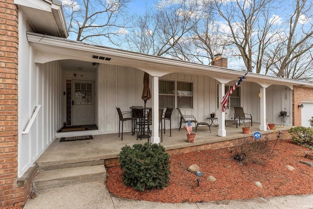 view of exterior entry featuring a chimney, a porch, board and batten siding, and brick siding