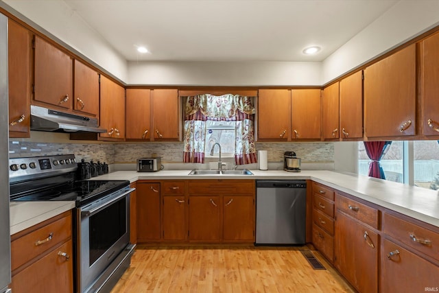 kitchen with stainless steel appliances, a sink, light countertops, and under cabinet range hood