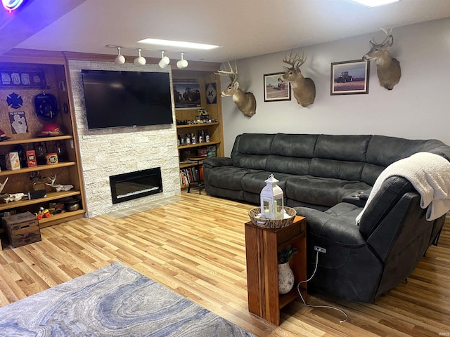 living area with built in shelves, wood finished floors, and a stone fireplace