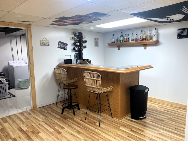 bar with a drop ceiling, wood finished floors, visible vents, a dry bar, and washer / dryer