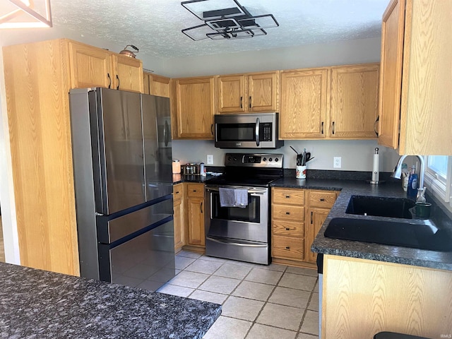 kitchen featuring light tile patterned floors, dark countertops, appliances with stainless steel finishes, a textured ceiling, and a sink