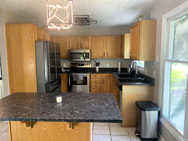 kitchen with a textured ceiling, a kitchen island, a sink, appliances with stainless steel finishes, and a kitchen bar