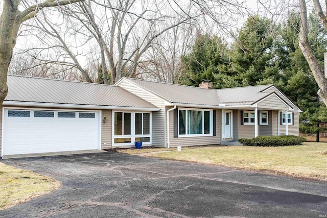 ranch-style house featuring metal roof, aphalt driveway, a garage, a chimney, and a front yard