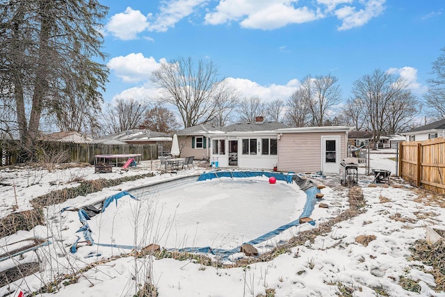 snow covered house with a trampoline, a fenced backyard, and a sunroom