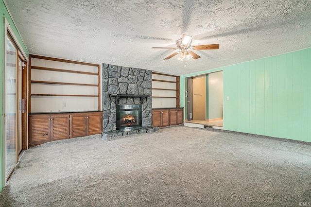 unfurnished living room featuring a textured ceiling, ceiling fan, built in shelves, a fireplace, and carpet