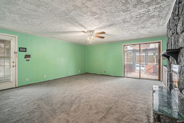 unfurnished living room featuring a textured ceiling, a stone fireplace, carpet flooring, and a ceiling fan