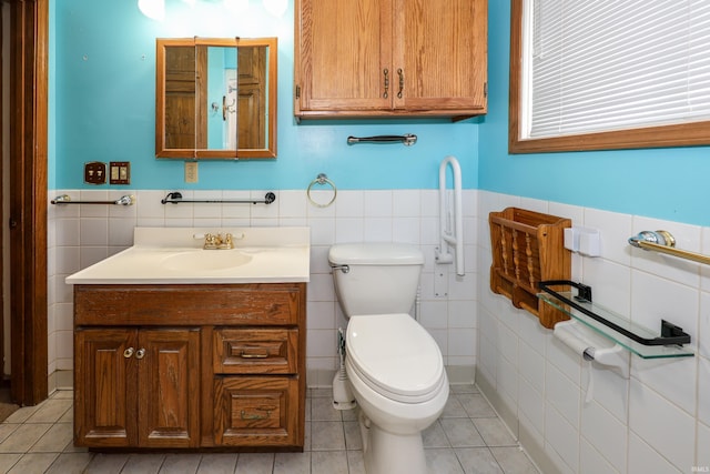 bathroom featuring wainscoting, toilet, tile patterned floors, vanity, and tile walls