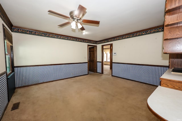 spare room featuring carpet, a wainscoted wall, visible vents, and ceiling fan