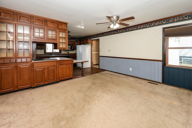 kitchen featuring white refrigerator with ice dispenser, visible vents, light colored carpet, a wainscoted wall, and brown cabinets