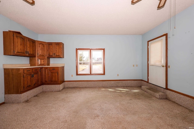 kitchen with light countertops, light colored carpet, brown cabinetry, ceiling fan, and a textured ceiling