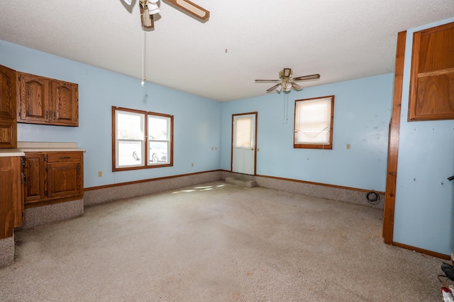 empty room featuring light carpet, ceiling fan, a textured ceiling, and baseboards