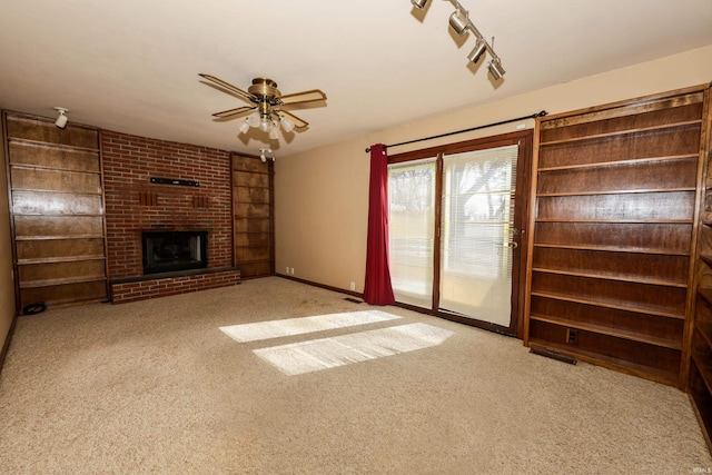 unfurnished living room featuring carpet floors, a fireplace, a ceiling fan, baseboards, and track lighting