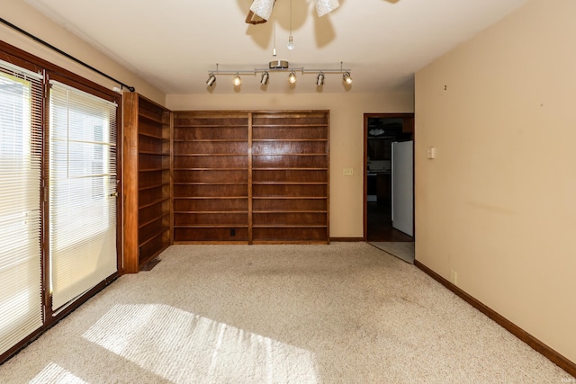 empty room featuring track lighting, baseboards, a ceiling fan, and light colored carpet